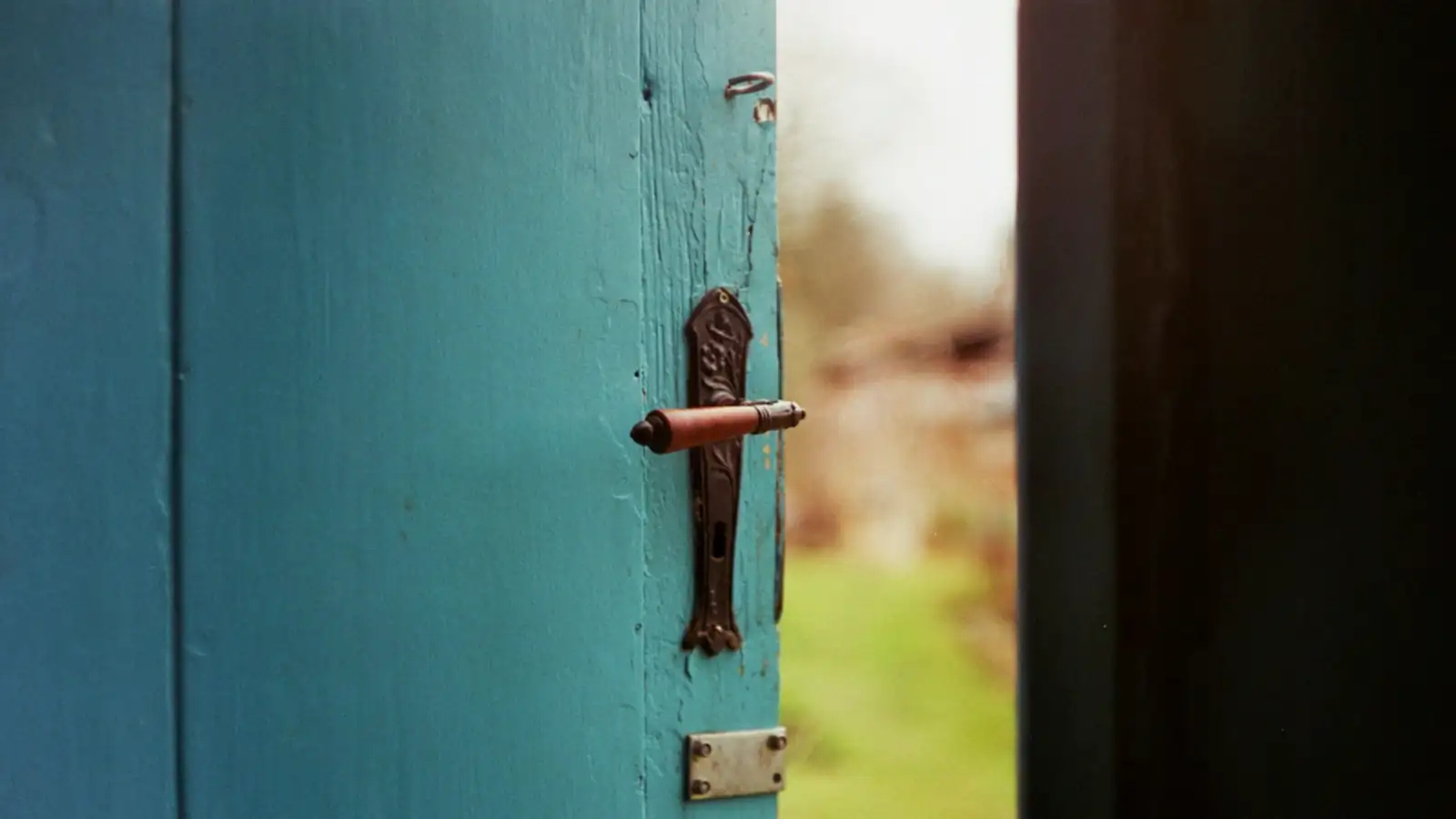 Puerta de madera pintada entreabierta, con su manilla de siempre